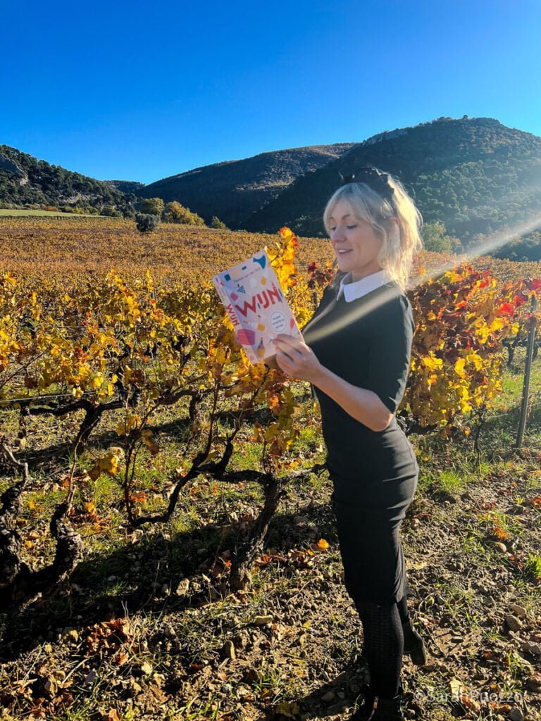 Sarah Puozzo die het boek Wijn leest tussen de wijnranken.