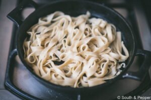 Verse pasta in een pan dat op smaak wordt gebracht met olijflie.